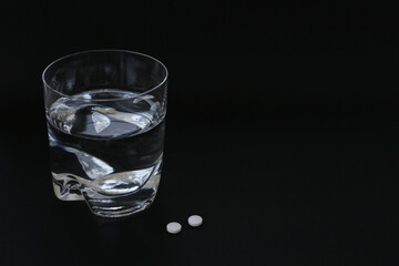 Glass of water and pills on black background, space for text