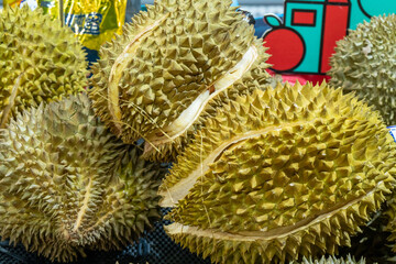 A pile of yellow durian fruit with green spines, cut open to reveal the soft and juicy interiors