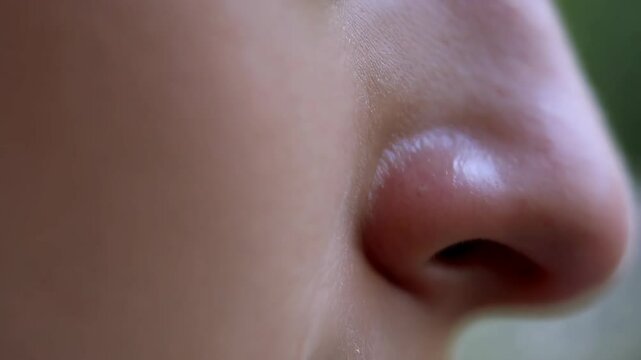 Close-up examination of a White person's nose as a tear slowly falls down their face showing skin texture and details in soft lighting