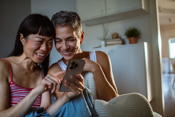 Smiling lesbian couple using smartphones together in bed