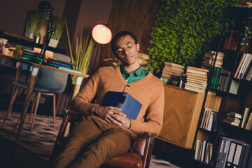 Young man resting with a book in cozy home study at evening