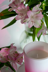 A close-up of a candle with Peruvian lilies in the background.