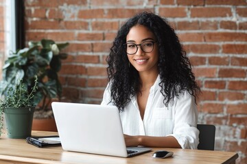 Young woman smiling using laptop at modern office. Female student working from home in bright workspace. Freelance business lifestyle concept