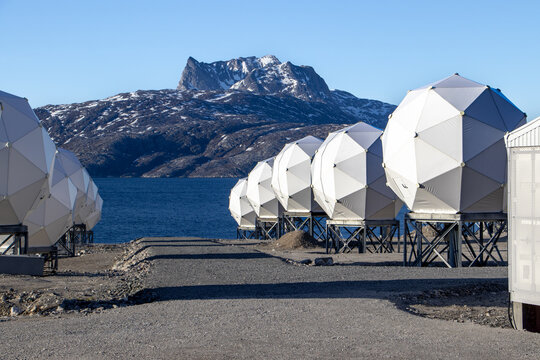 Radar and satellite domes near the coast of Greenland with a scenic view of mountains and ocean