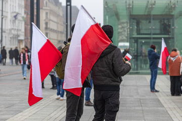 People holding Polish flags during a peaceful public gathering in a city square with modern and...