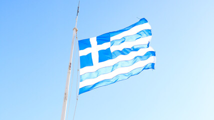 Bandeira da Grécia hasteada em Atenas, diante de um céu claro e os monumentos históricos da...