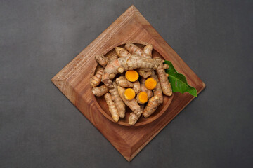 Fresh turmeric root and slices on wooden plate isolated on black background. High resolution photo.