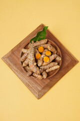 Fresh turmeric root and slices on wooden plate isolated on yellow background. High resolution photo.