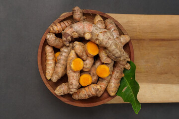 Fresh turmeric root and slices on wooden plate isolated on black background. High resolution photo.