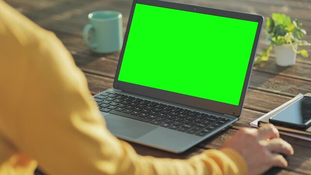man using the laptop with green screen on the wooden table outdoor,back view of male at computer using mouse scrolling browsing internet online