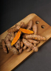 Fresh turmeric root and slices on wooden plate isolated on black background. High resolution photo.