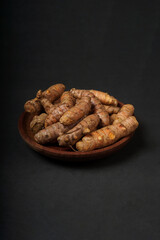 Fresh turmeric roots on wooden plate isolated on black background. High resolution photo.