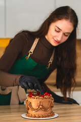 Close-up. Beautiful female confectioner decorates a chocolate cake with cherries.