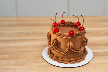 A chocolate holiday cake decorated with a cream pattern and a cherries.