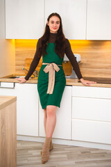 A vertical portrait of a smiling female confectioner in a green apron in her kitchen.