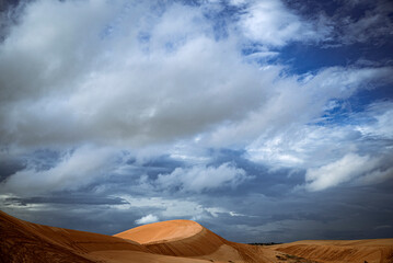 A desert landscape with a hill and a cloudy sky