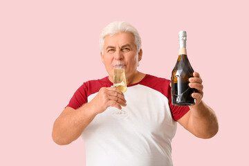 Senior man with bottle and glass of champagne celebrating Christmas on pink background