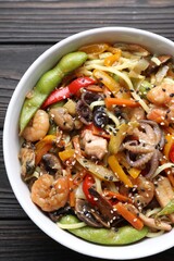 Stir-fry noodles with sea food in bowl on wooden table, top view
