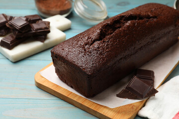 Tasty sponge cake and pieces of chocolate on light blue wooden background, closeup