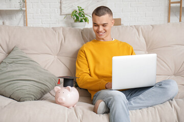 Male student with piggy bank and laptop on sofa in room. Concept of savings for education