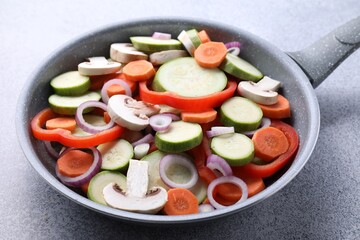 Frying pan with mix of fresh vegetables and mushrooms on grey table, closeup