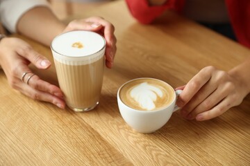 Women with cups of delicious coffee drinks at wooden table in cafe, closeup