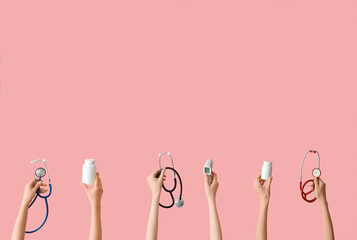 Female hands with stethoscopes, pills and thermometer on pink background