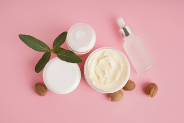 Jar with shea butter and cosmetics products on pink background