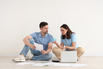 Young couple sitting on floor with empty piggy bank and laptop at home. Concept of bankruptcy