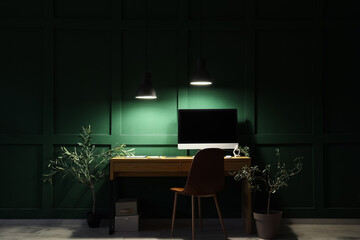 Stylish workplace with modern computer near green wall in office at night