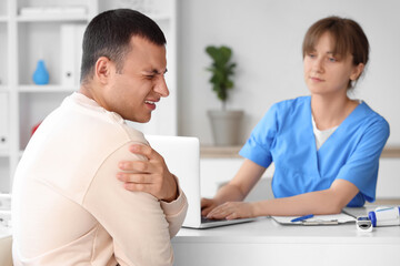 Obraz premium Young man with pain in his shoulder visiting doctor at hospital