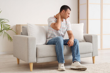 Obraz premium Young man suffering from pain in his neck on sofa at home