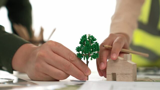 A video of architect using tree and home model to measure blueprint. Architect designing house construction on a table at studio, with architectural plan scattered around. Focus on hand. Delineation.