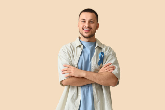 Young man with blue ribbon on beige background. Prostate cancer awareness concept