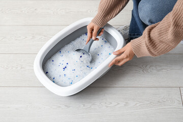 Woman with scoop cleaning litter box for cat on floor in room
