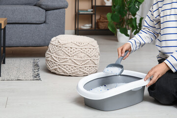 Woman cleaning litter box for cat on floor in room