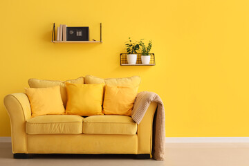 Shelf with books and modern safe hanging on yellow wall in living room