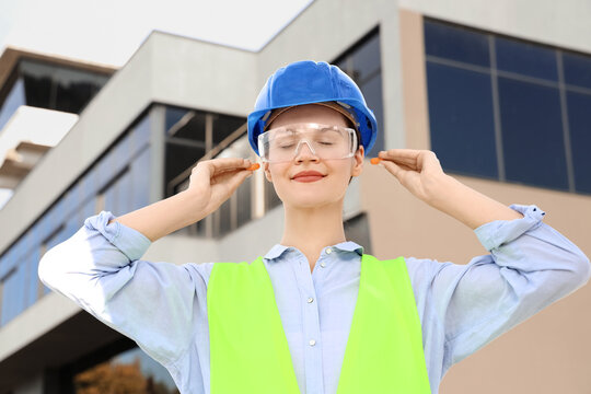 Female builder inserting earplugs outdoors