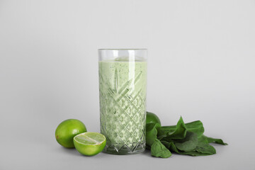 Glass of fresh spinach smoothie with limes on grey background