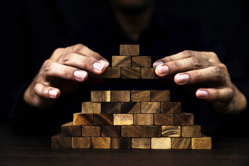 Hand placing wooden block stack in pyramid tower carefully to prevent collapse or crash concepts of...