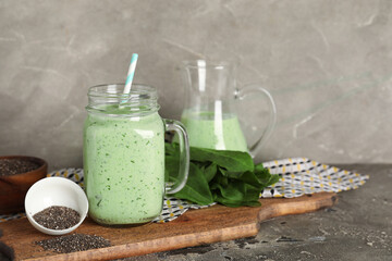 Mason jar of fresh spinach smoothie and bowl with chia seeds on grey background