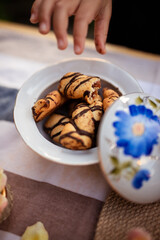 Little hand of a little girl wants to take a cookie. Plate full of cookies. A table is served and decorated with a beautiful porcelain set of dishes decorated with blue flowers.