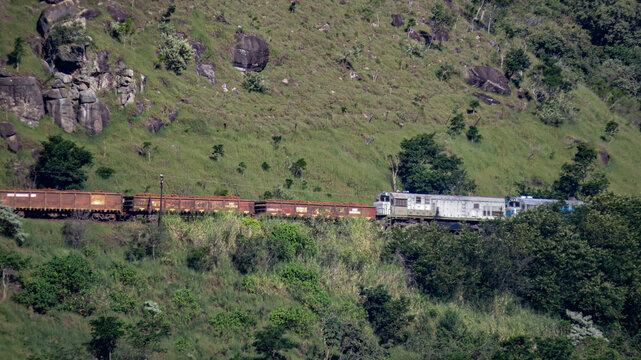 A mining transport train loaded with ore, moving through a vast industrial landscape. The train's heavy cargo contrasts against the expansive background, showcasing mining operations.