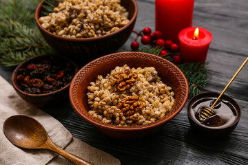 Bowls of traditional Ukrainian Kutya dish with Christmas tree branches and burning candles on black wooden background