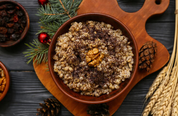 Bowl of traditional Ukrainian Kutya dish with pine cones and Christmas tree branch on black wooden background