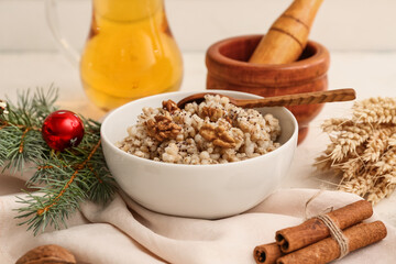 Bowl of traditional Ukrainian Kutya dish with Christmas tree branch and jug of uzvar on white table
