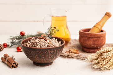 Bowl of traditional Ukrainian Kutya dish with Christmas tree branches and jug of uzvar on white table