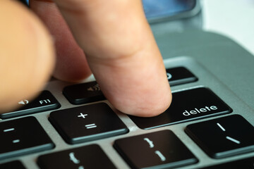 Finger of the computer user, he presses the delete button on the computer keyboard	
