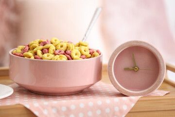 Pink alarm clock with cereal rings on tray in bedroom, closeup