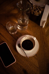 Cup of coffee on the wooden table in cafe. Glass bottle of water. Dark mood